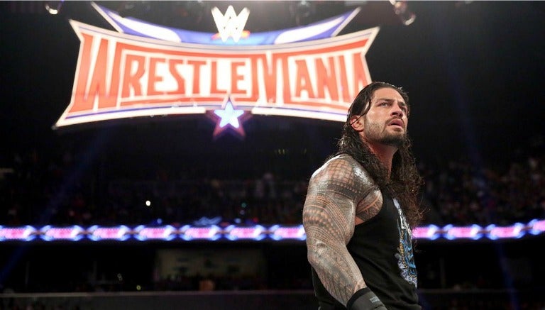 Roman con el logo de Wrestlemania de fondo