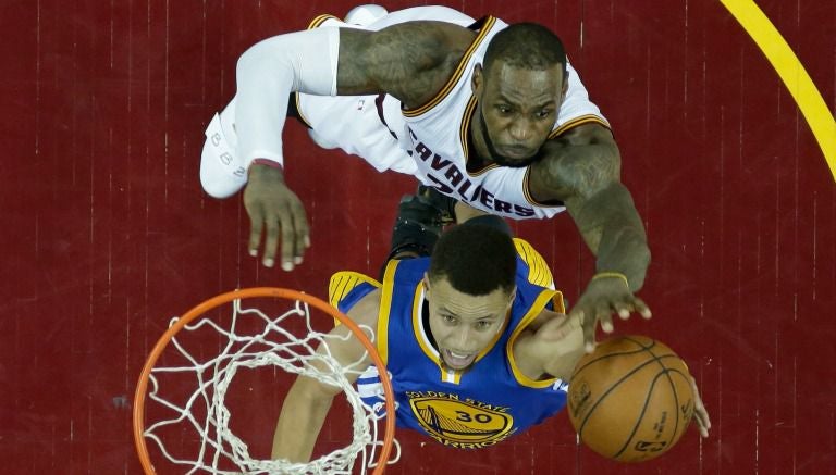 Stephen Curry avanza hacia la canasta mientras LeBron James intenta quitarle el balón 