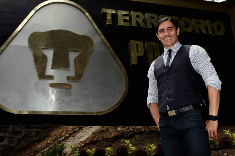 Paco Palencia junto al escudo de Pumas