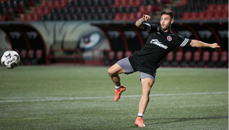 Héctor Villalba intenta patear un balón con la playera de Xolos