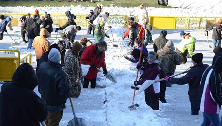 Aficionados quitan la nieve de las tribunas del Lambeau Field