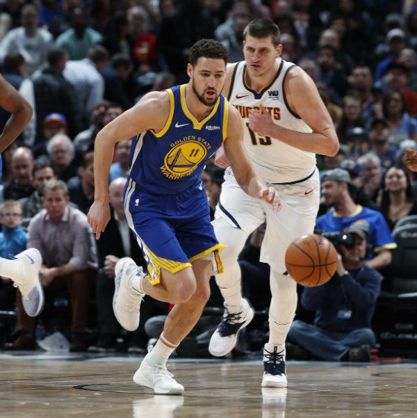 Klay Thompson lleva un balón mientras que Nikola Jokic lo sigue