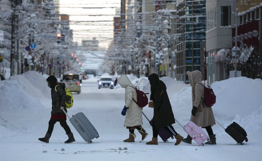 Grupo de turistas cruza una calle nevada con sus maletas en Sapporo