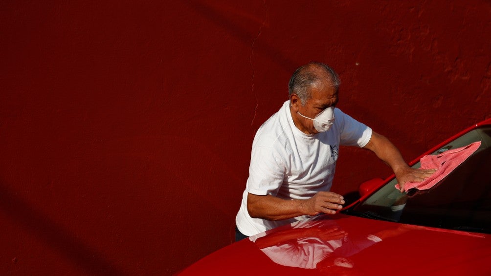 Persona limpia su coche usando cubrebocas