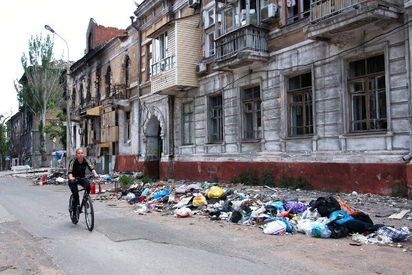 mujer pasa en bicicleta por delante de un edificio dañado