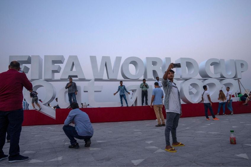 Turistas tomándose una foto en un letrero de Qatar 2022