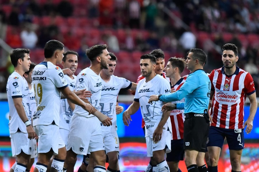 Jugadores de Pumas y Chivas rodeando al árbitro