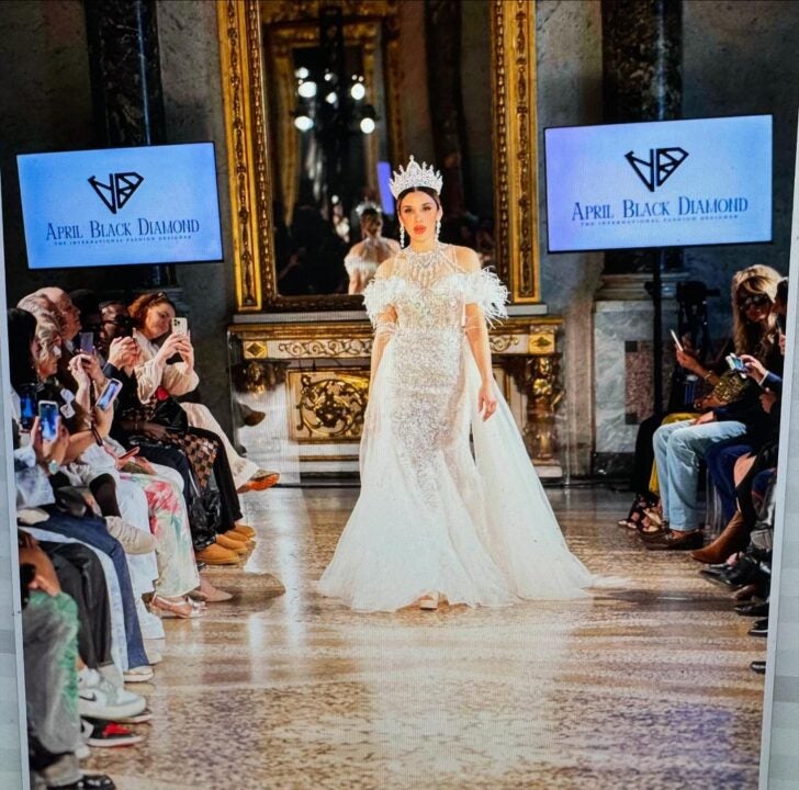 Emma Coronel posando con un vestido blanco y corona para el Fashion Week